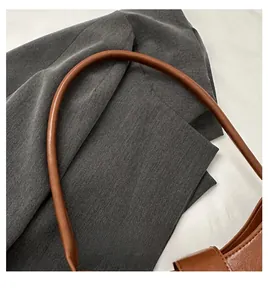 Detail of a brown leather handbag handle over a grey textured fabric suit jacket