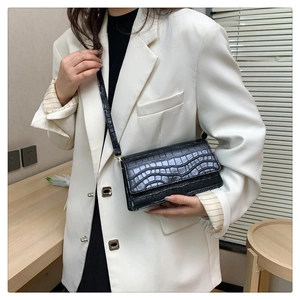 Detail of black crocodile texture bag styled with a white blazer for a chic look