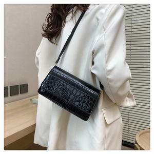 Detail of black crocodile texture shoulder bag on white blazer with leather strap