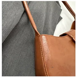 Detail view of brown glossy leather shoulder bag showing fine texture and sewing craft