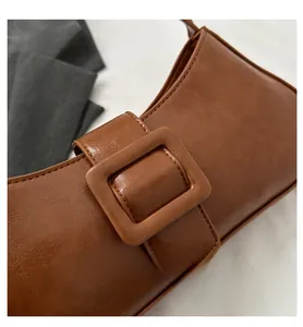 Close-up of brown leather shoulder bag with textured finish and large square buckle detail