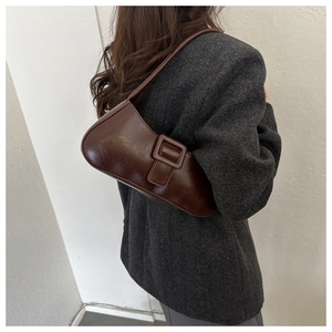 Detail of dark brown leather underarm bag with decorative belt buckle on model