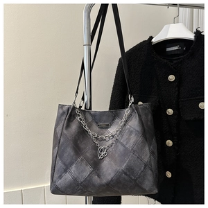 Detail of grey denim quilted tote bag with silver chain straps and metallic logo plate