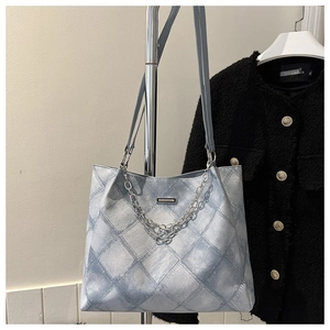 Detail of light blue denim tote with diamond pattern, silver chains and metal logo plate