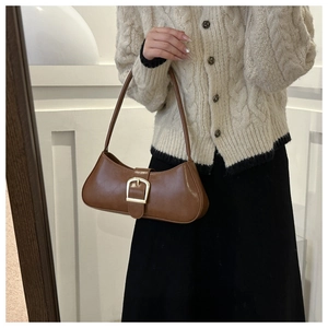 Brown retro underarm bag with gold buckle worn on a beige tweed cardigan