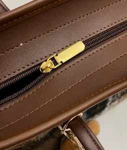 Detailed view of the smooth golden metal zipper and brown leather stitching on tote bag