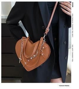 Detail of brown heart-shaped leather bag with silver chains and metallic cross pendant