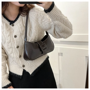 Detail of dark brown leather underarm bag with belt buckle on a model's shoulder
