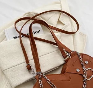 Detail of a brown leather heart-shaped bag with silver chain and metal stud accents