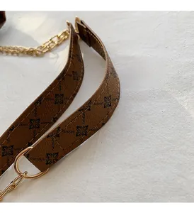 Detail of brown faux leather strap with black monogram pattern and gold metal chain links