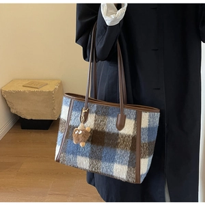 Detail of wool plaid tote bag with brown leather handles and plush monster charm