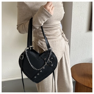 Detail of a black heart-shaped leather bag featuring silver metal rivets and chain strap