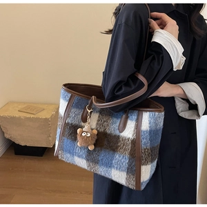 Detail of checkered wool tote bag with brown leather handles and plush monster charm