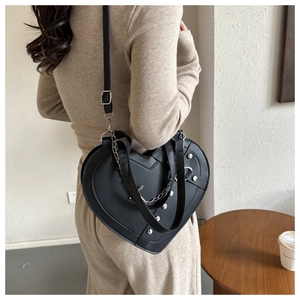 Detail of black heart-shaped crossbody bag with silver studs and chain on a model
