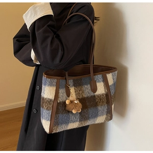 Detail of wool plaid tote bag featuring brown leather straps and plush bear pendant
