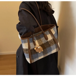 Detail of checkered tote bag with brown leather handles and plush bear charm on model