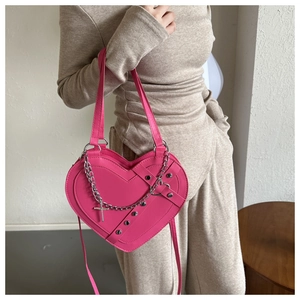 Detail of pink heart-shaped bag with silver chain, cross pendant and metal studs