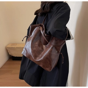 Détail du grand sac cabas en cuir marron foncé avec cordon de serrage porté par le modèle