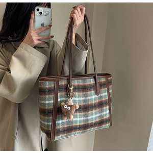 Detail of plaid wool tote bag featuring brown leather trim and cute plush bear charm