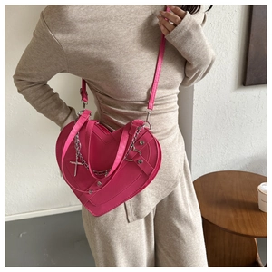Detail view of pink heart-shaped crossbody bag with silver cross charm and metal chains