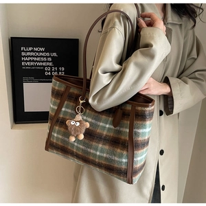 Detail of wool plaid tote bag with brown leather handles and a plush monster charm