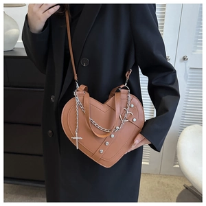 Detail of a brown heart-shaped crossbody bag with silver chains, studs and cross charms