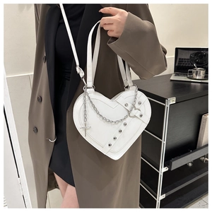 Detail of white heart-shaped bag with silver studs, metal chains and cross pendant