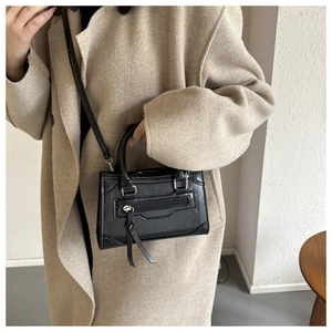 Detail showing the textured black leather crossbody bag paired with a beige wool coat