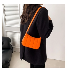 Detail der orangefarbenen gesteppten Schultertasche mit Gitterstruktur vor schwarzem Blazer