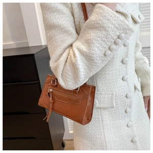 Detailed view of a brown vintage crossbody bag with long tassels on a tweed coat