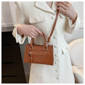 Detail of a brown leather crossbody bag with tassel zipper and adjustable strap