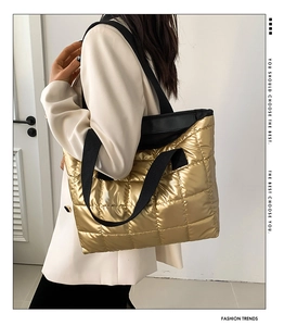 Detail of metallic gold quilted tote bag with black straps worn by model for daily commute