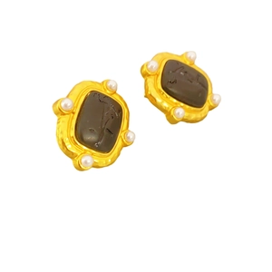 Boucles d'oreilles baroques dorées avec relief noir et perles blanches sur fond blanc neutre