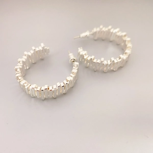 Detail view of silver C-shaped hoop earrings featuring a unique jagged geometric texture