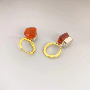 Detailansicht der silbernen Ohrringe mit leuchtend orangen Kristallen und Goldringen