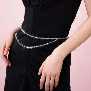 Minimalist transparent crystal body chain layered on a black dress with pink background
