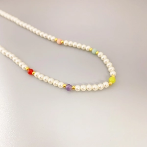 Minimalist pearl necklace with colorful beads and golden accents on grey surface