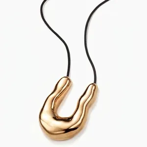 Macro shot of minimalist gold irregular U-shape pendant with polished mirror finish