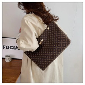 Brown monogram tote bag with gold chain strap worn by a model in a trench coat