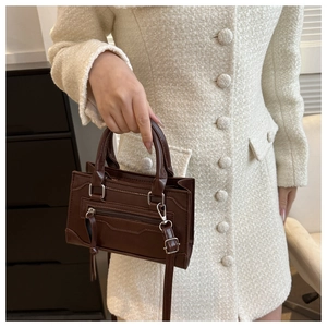 Detail of dark brown leather handbag featuring silver hardware and long tassel zippers