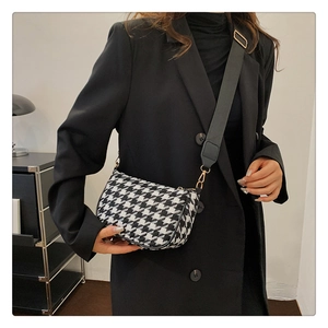 Close-up of houndstooth crossbody bag with black wide strap and gold hardware buckles