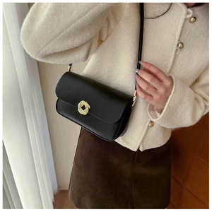 Sac à bandoulière en cuir noir avec boucle dorée porté par un mannequin chic