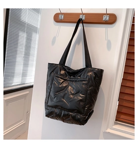Detail of black quilted puffer tote bag with diagonal stitching hanging on a wooden hook