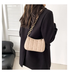 Detail einer beigen gesteppten Filzschultertasche mit goldener Kette auf einem schwarzen Blazer