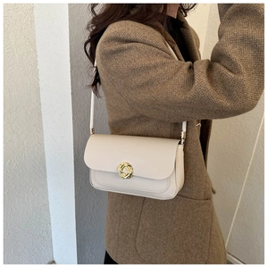 Detailed close-up of a minimalist cream shoulder bag with a gold round knot metal buckle
