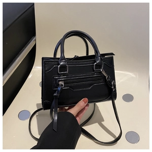Detail of black faux leather handbag featuring silver zippers and long fringe tassels