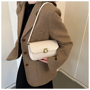 Close-up of cream shoulder bag with golden round metal buckle on a tweed blazer