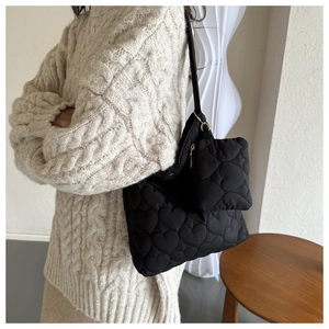 Détail du sac cabas matelassé cœur noir avec sa pochette sur un pull en maille torsadée