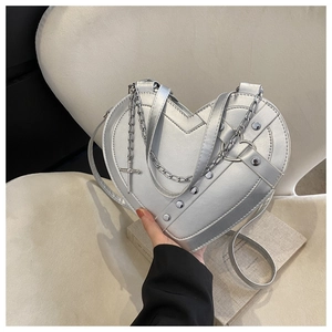 Close-up detail of silver heart bag with metallic rivets, cross charm and chain strap