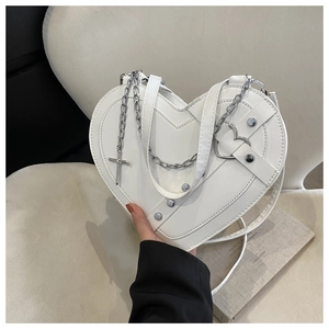 Close-up of white heart-shaped leather bag with silver cross charm and rivet details
